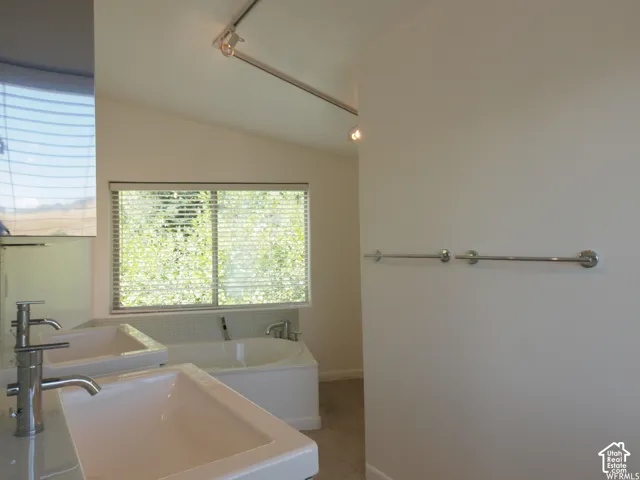 Dual vanity featuring rectangular vessel sinks and metal faucets, soaking tub with tile surround, and overhead track lighting