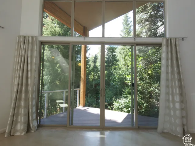 Floor-to-ceiling multi-panel windows, sliding glass door, exposed wooden structural beam, and expansive exterior deck with cable railing