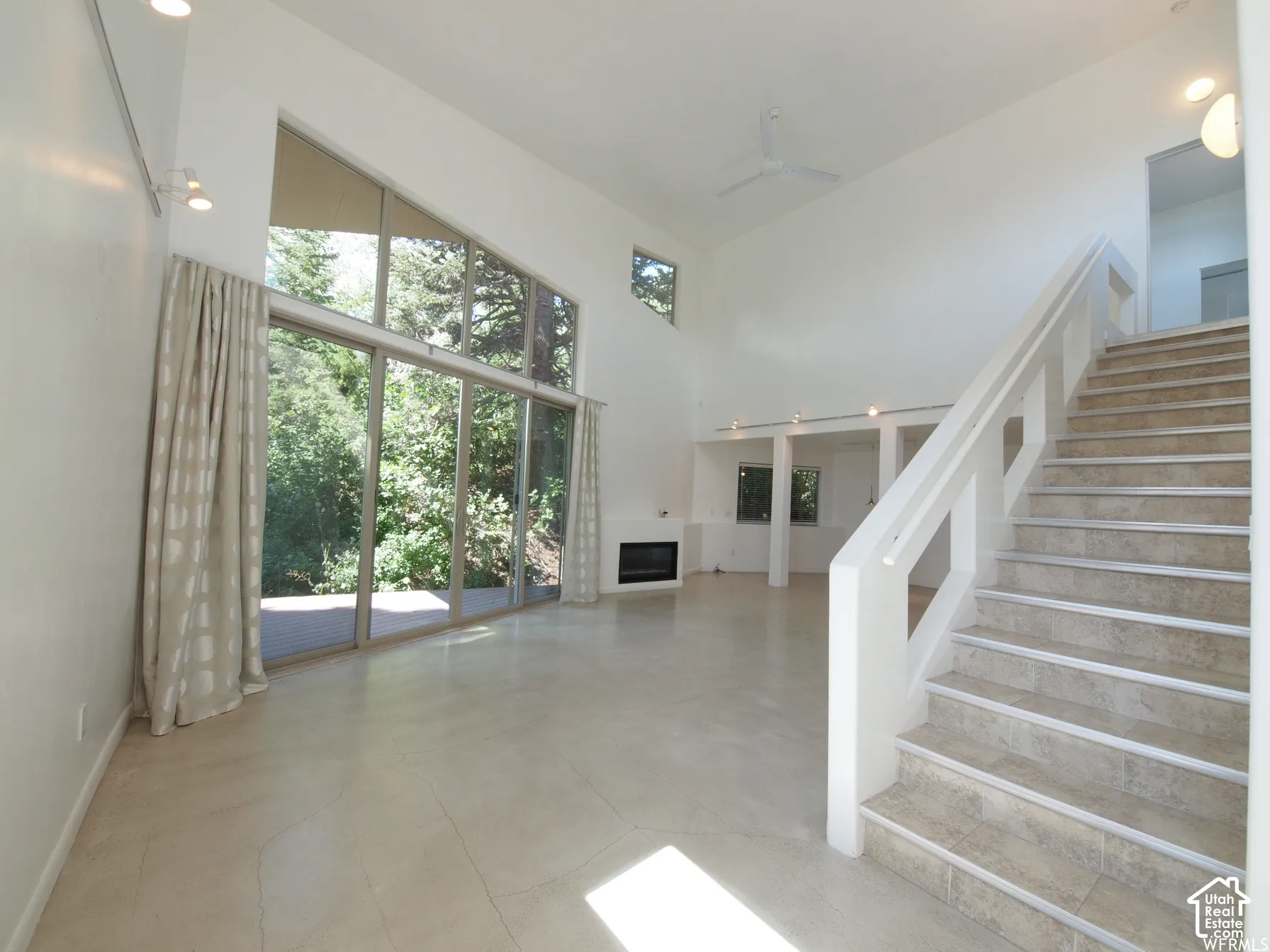 Open-concept interior featuring double-height ceilings, floor-to-ceiling glass sliding doors, stone-tiled staircase, and a recessed fireplace
