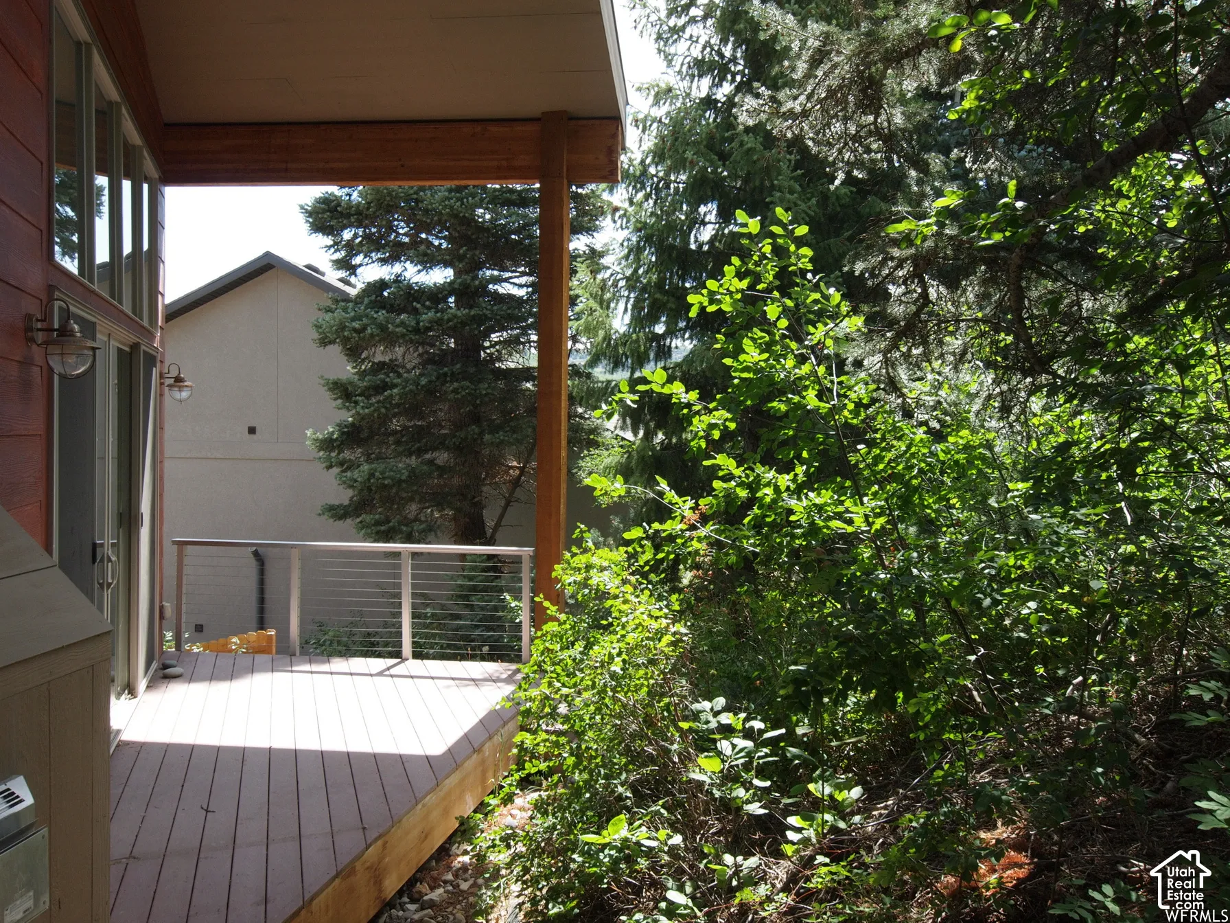 Covered deck featuring wood-finish decking, metal cable railing, and expansive glass exterior paneling