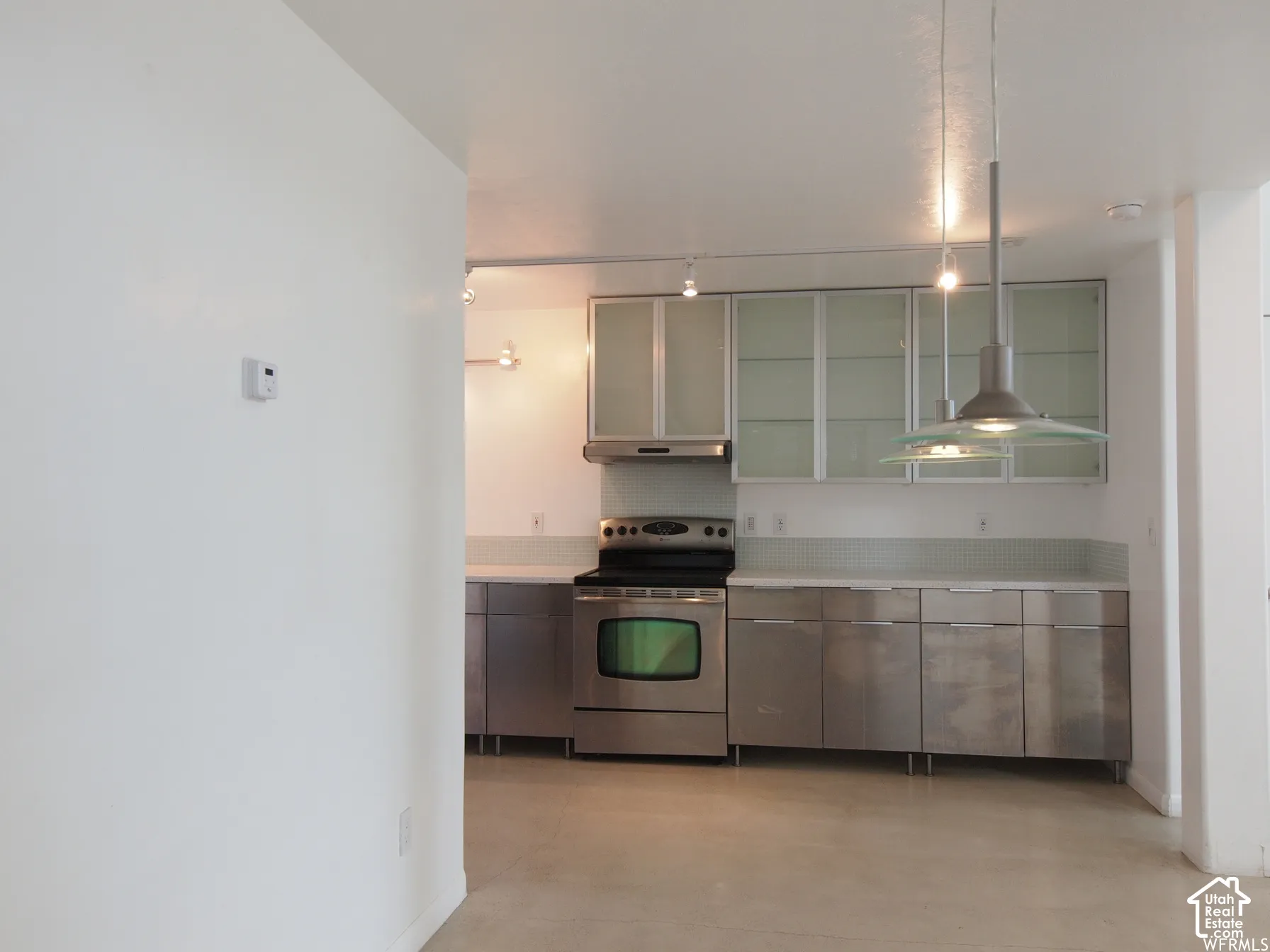 Kitchen featuring stainless steel cabinetry, frosted glass-panel upper cabinets, polished concrete flooring, stainless steel range, and dual pendant lighting