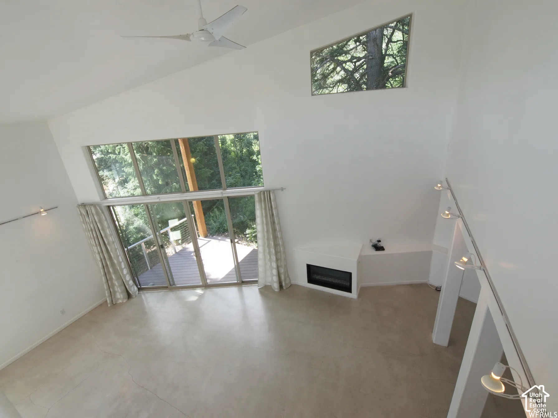 Vaulted ceiling with a white ceiling fan, floor-to-ceiling windows, built-in fireplace, clerestory window, and track lighting