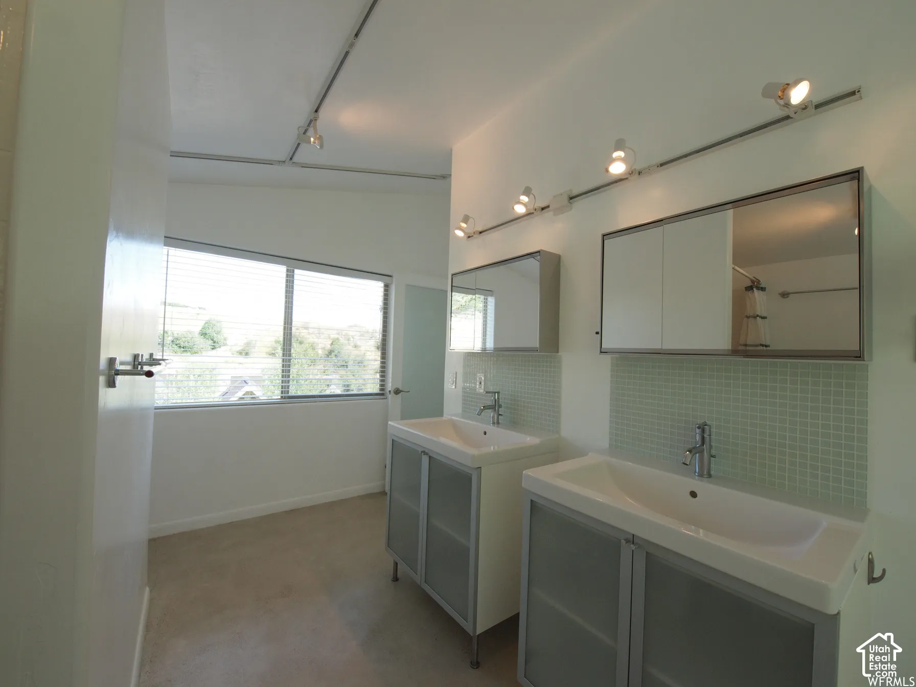 Dual vanity featuring frosted-glass cabinet doors, integrated rectangular sinks, mint-green square tile backsplashes, and adjustable track lighting