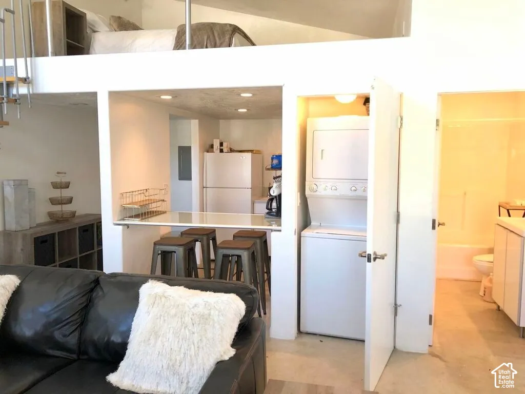 Multi-level interior featuring an elevated loft, a built-in kitchen peninsula, recessed ceiling lighting, a dedicated closet with stacked laundry appliances, and a bathroom with a tub-shower combination