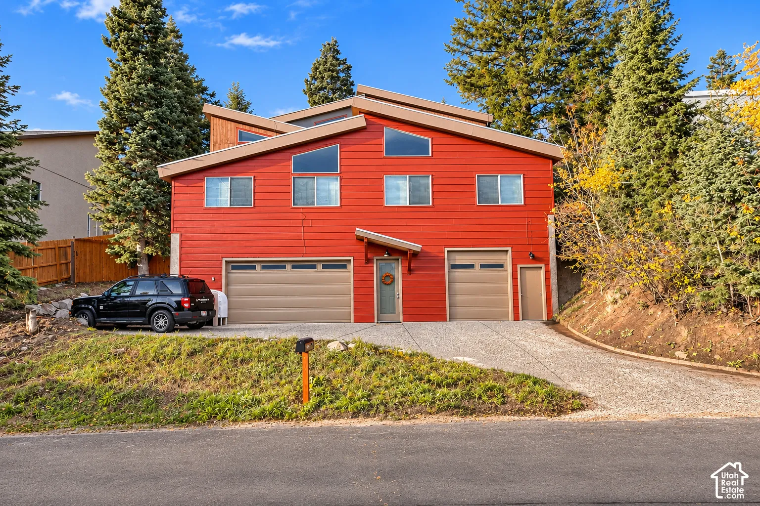 Multi-level exterior featuring horizontal wood siding, shed rooflines with geometric windows, two attached garages, and a paved driveway