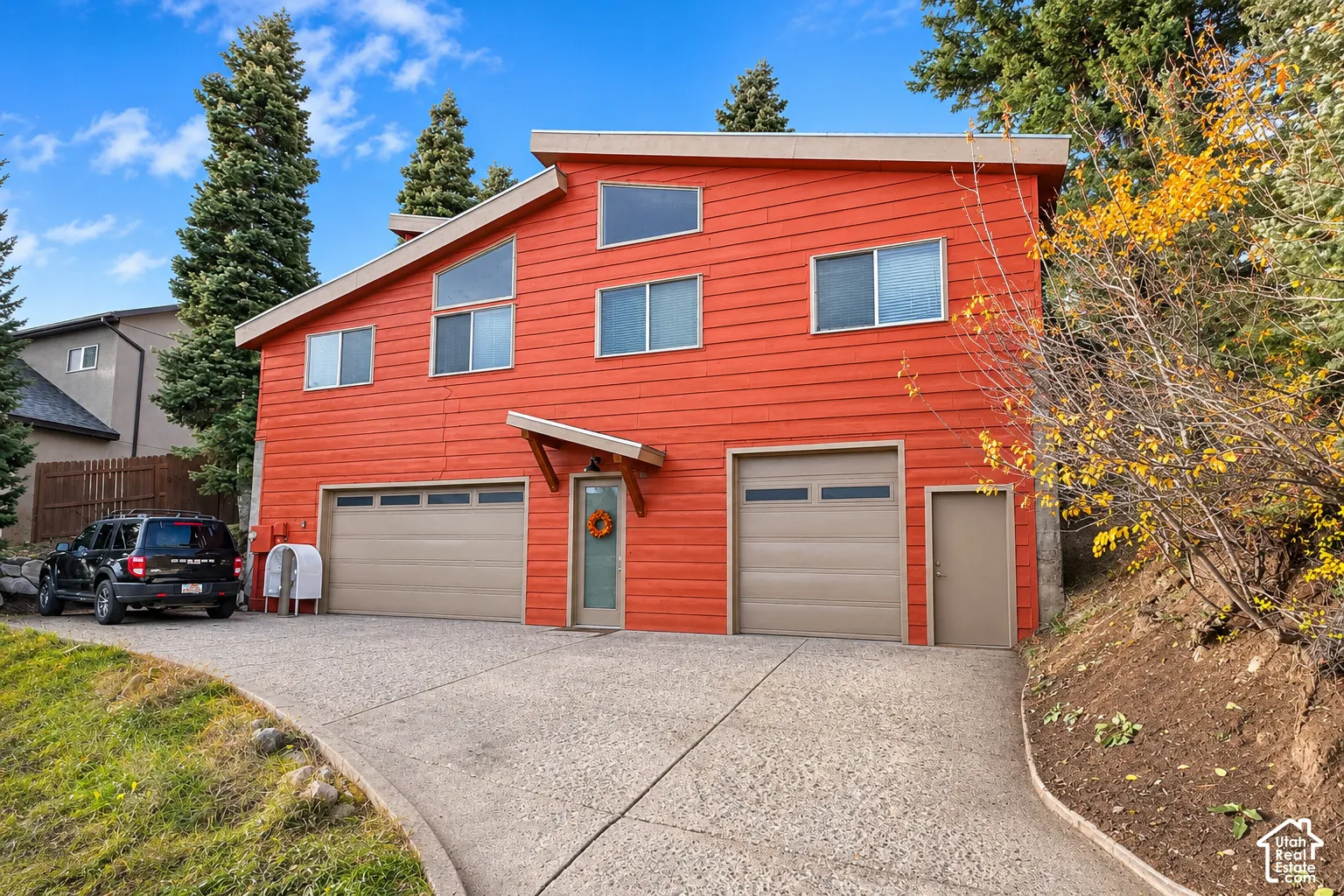 Contemporary exterior featuring horizontal lap siding, a pitched roofline with multi-level windows, a three-car garage configuration, and an expansive concrete driveway