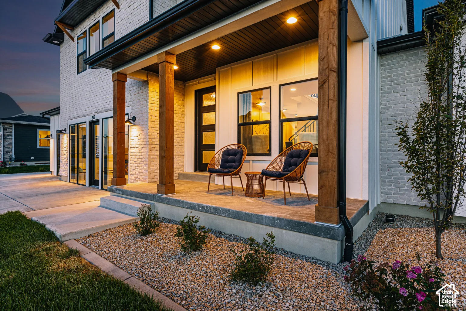 Covered front porch featuring textured brick veneer, stained wood support columns, concrete masonry, and modern paneled front door