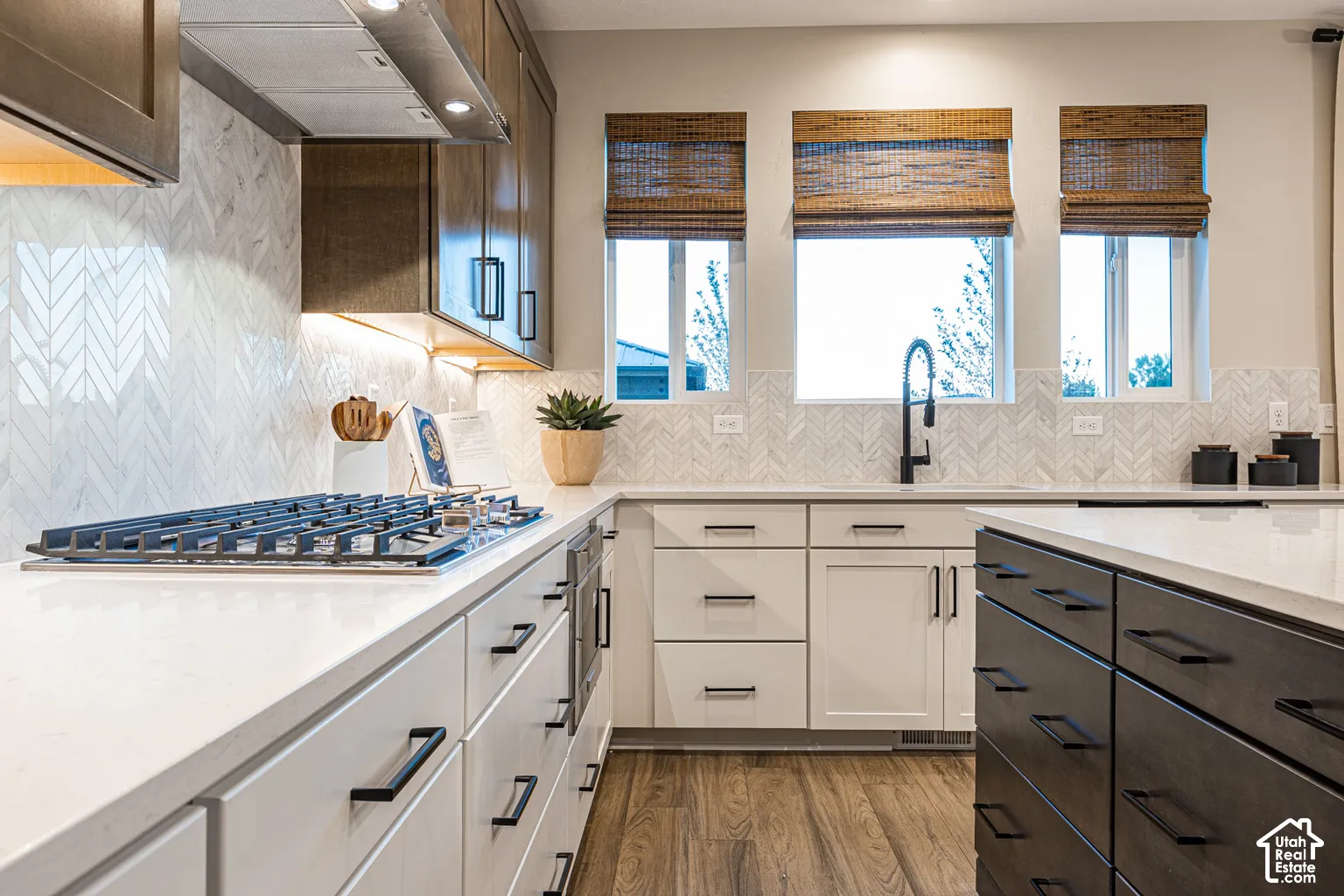 Kitchen featuring quartz countertops, herringbone-patterned tile backsplash, wood-finish cabinetry with matte black hardware, integrated stainless steel gas cooktop, and undermount sink with a matte black faucet