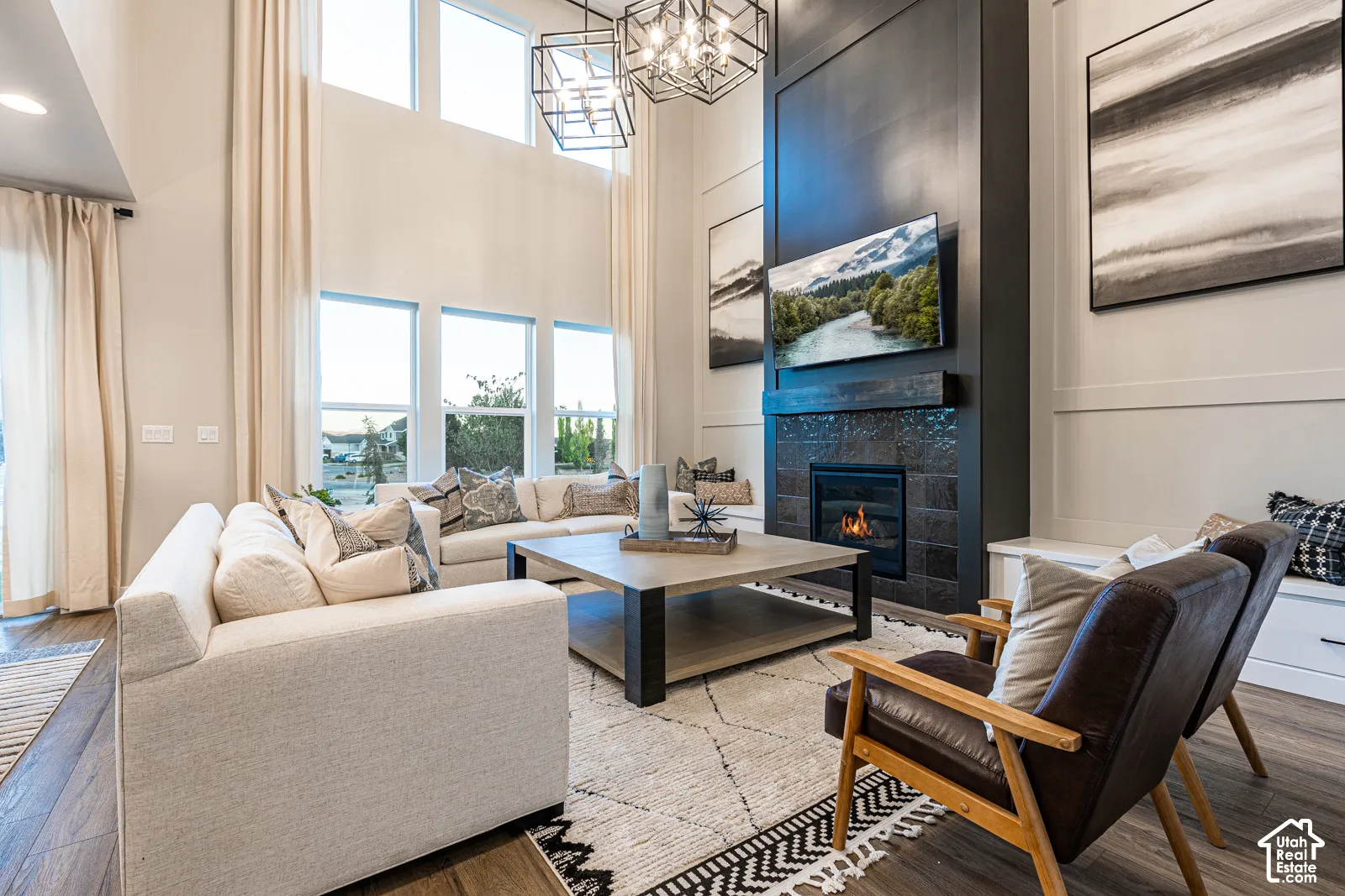 Double-height ceilings, floor-to-ceiling windows, floor-to-ceiling paneled fireplace wall, tiled fireplace surround with integrated hearth, and geometric chandeliers