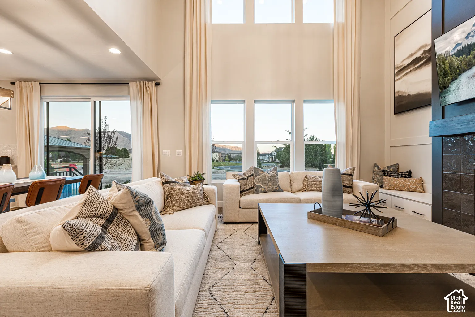 Two-story ceilings with expansive multi-pane windows, floor-to-ceiling fireplace with dark tile surround, built-in cabinetry, sliding glass door, and recessed lighting