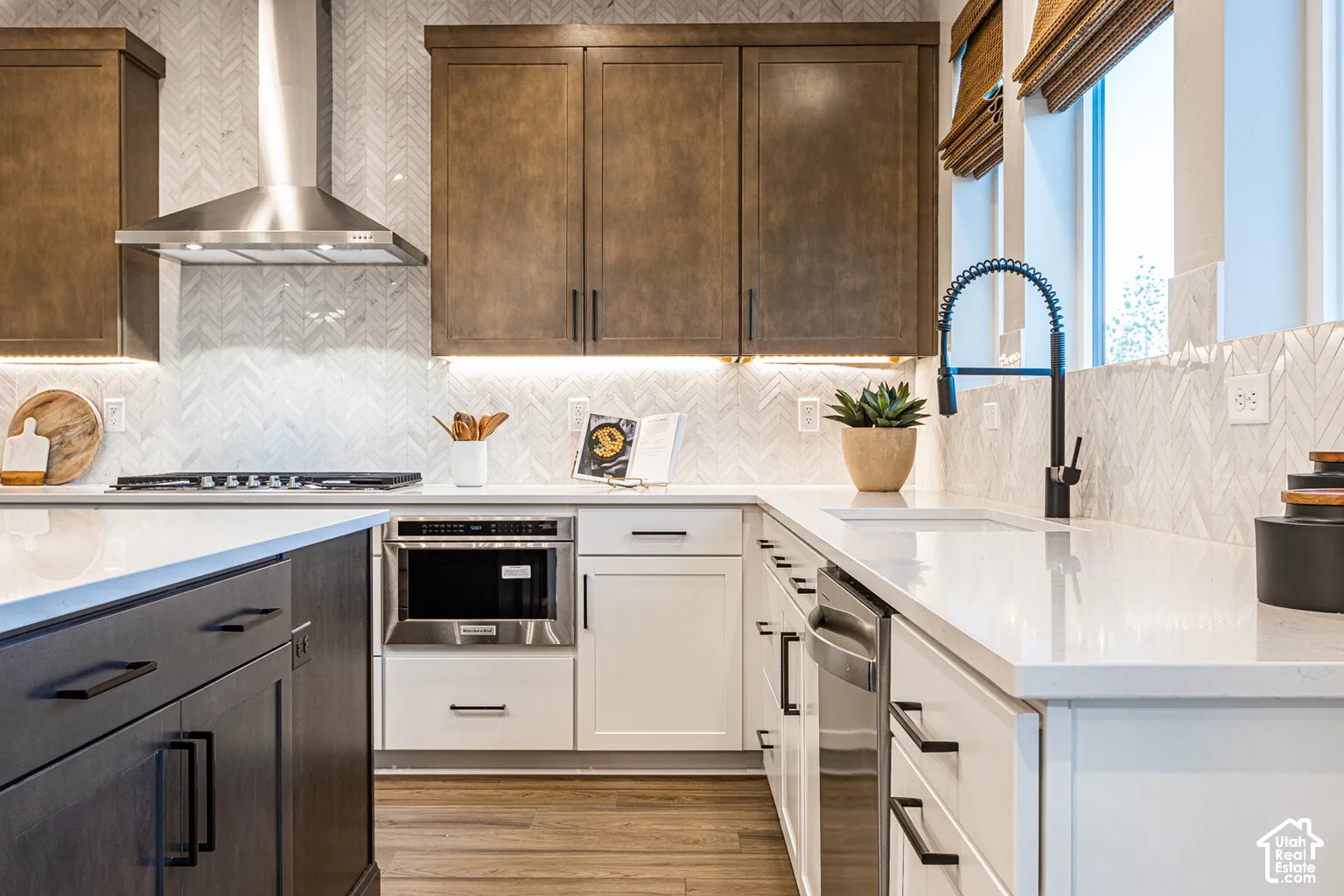 Kitchen featuring two-tone custom cabinetry, stone-surface countertops, a herringbone-pattern tile backsplash, stainless steel appliances, and matte black hardware