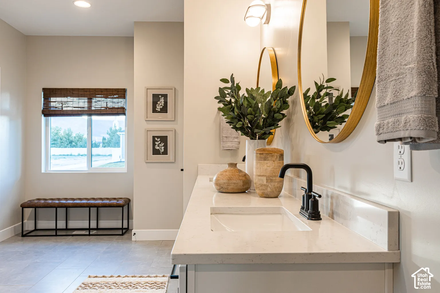 Double vanity featuring a light-toned countertop with an integrated rectangular sink and matte black faucet, accented by circular gold-rimmed wall mirrors and recessed lighting