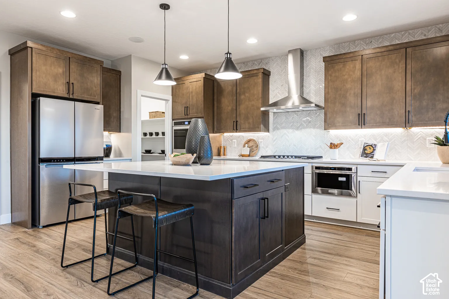 Kitchen featuring wood-finish cabinetry, central island with a quartz countertop, herringbone-patterned tile backsplash, stainless steel appliances, and pendant lighting