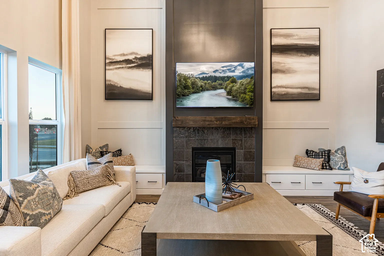 Double-height ceilings, floor-to-ceiling fireplace with stone tile surround, heavy timber mantel, and custom built-in cabinetry with drawer storage