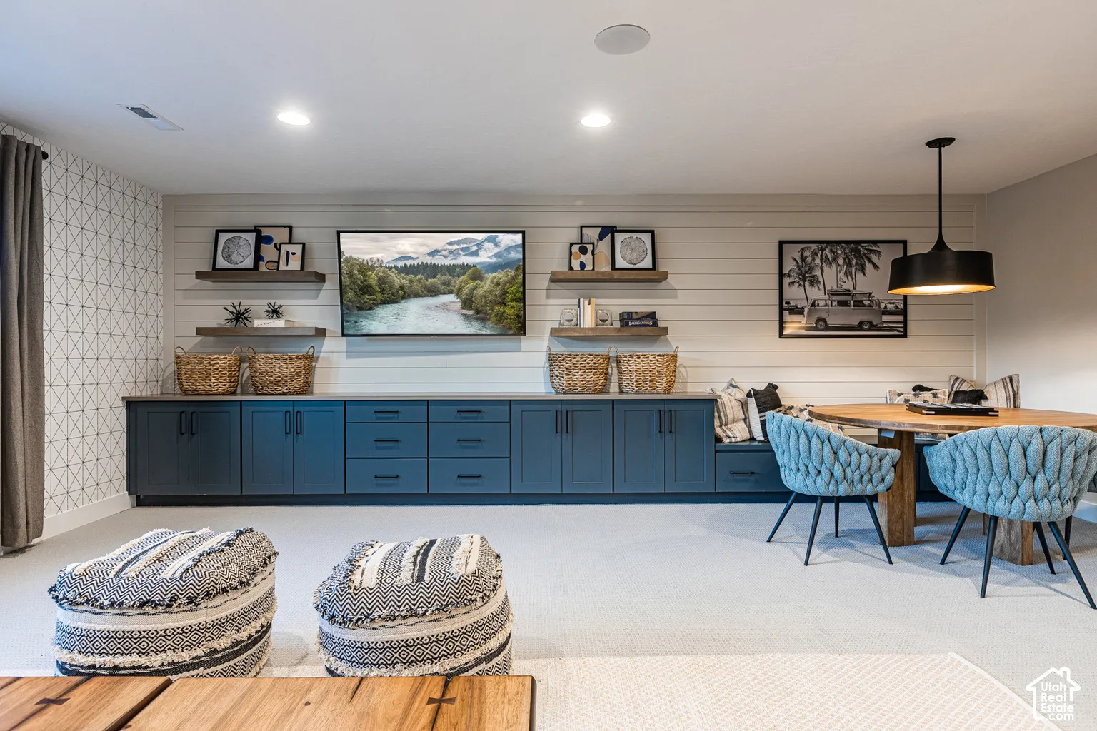 Custom blue-toned cabinetry with integrated drawers, horizontal shiplap wall detail, built-in wooden floating shelves, and an overhead pendant light fixture