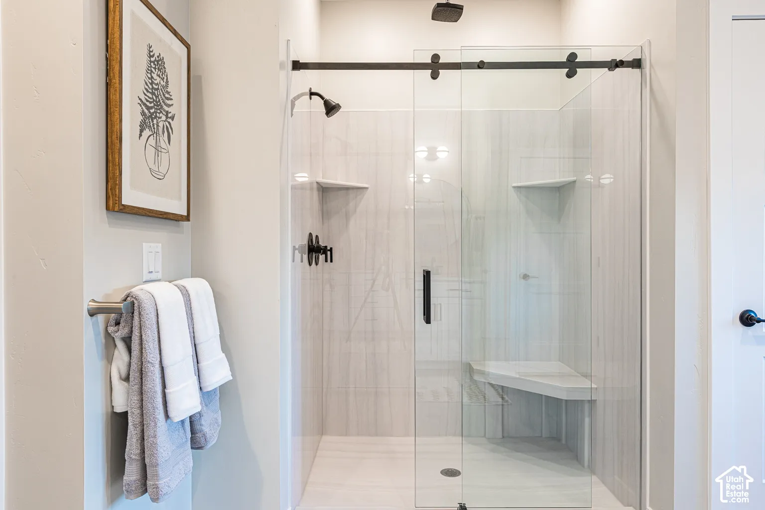 Walk-in shower featuring floor-to-ceiling tile, frameless glass sliding door, built-in corner bench, rainfall shower head, and matte black fixtures