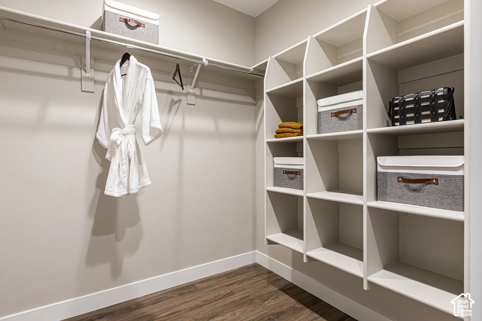 Walk-in closet featuring wood-finish flooring, floor-to-ceiling built-in shelving, and a continuous hanging rod