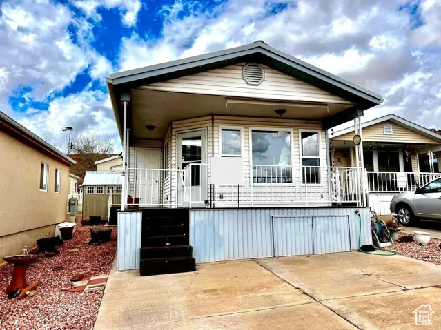 Exterior featuring vinyl siding, a covered front porch with a white metal railing, and a concrete driveway