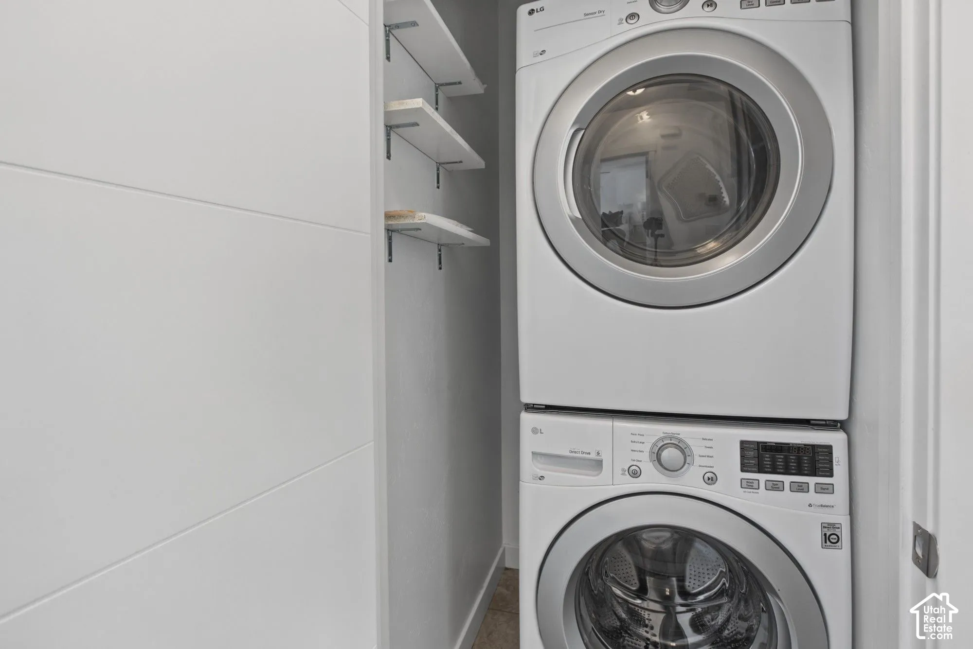 Stacked laundry unit featuring white front-load appliances and integrated wall-mounted shelving