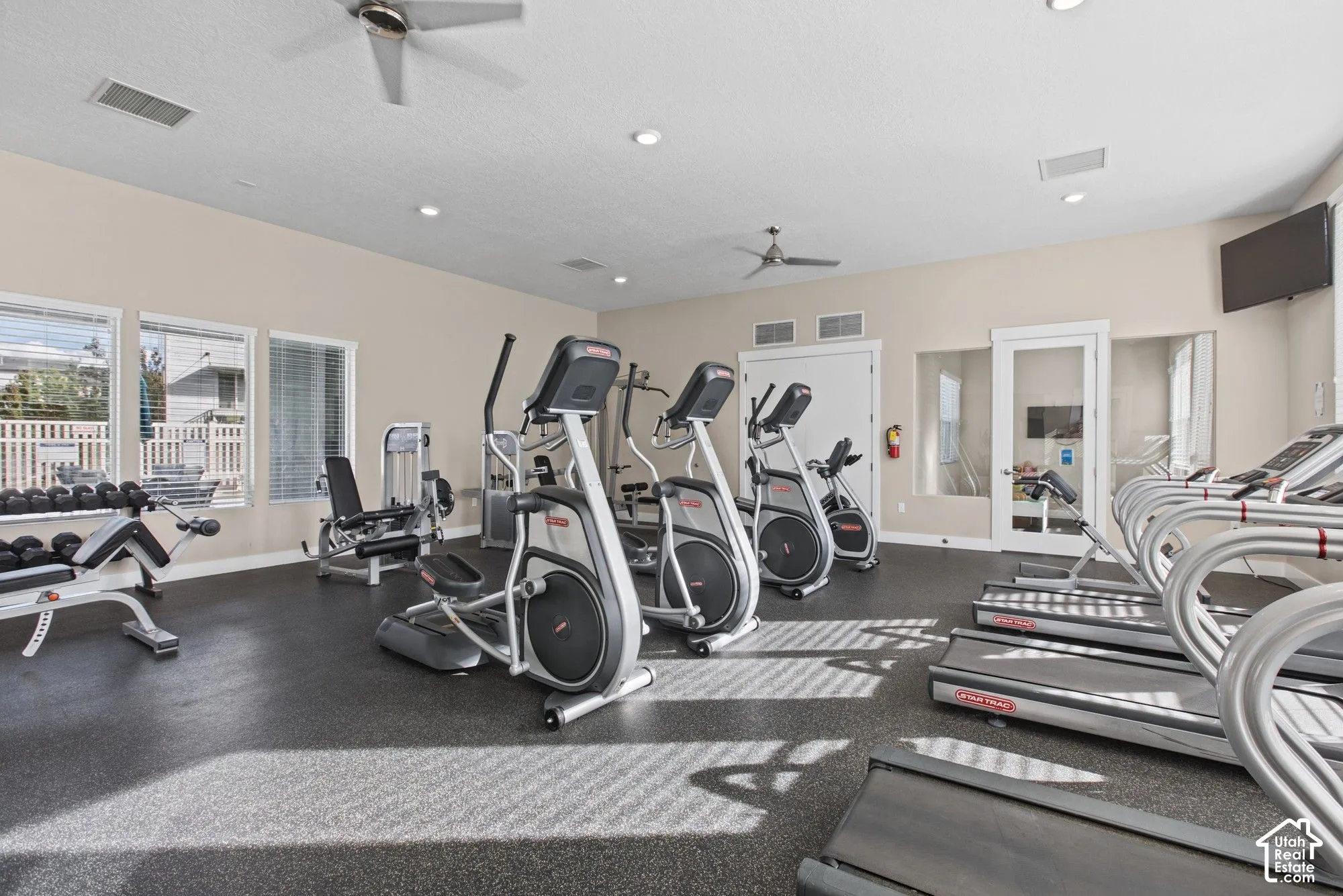 Fitness center featuring rubberized flooring, multiple windows with blinds, recessed lighting, and dual ceiling fans