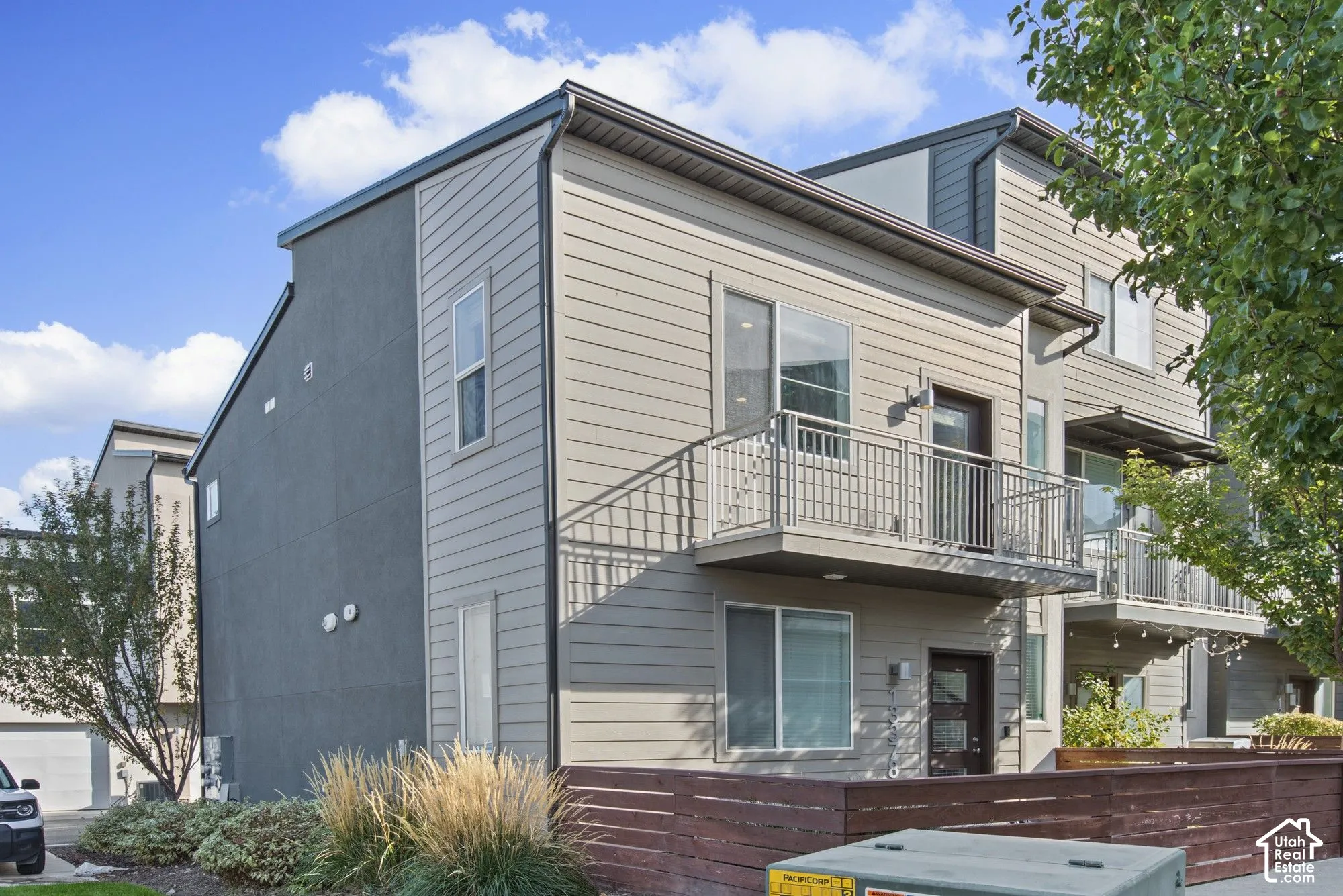 Modern multi-level exterior featuring horizontal lap siding, a private second-story balcony with metal railing, and a wood-slat privacy fence
