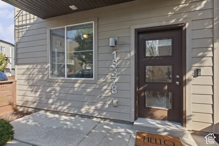 Horizontal lap siding exterior with a dark-finish entry door featuring three glass inserts, brushed metal house numbers, and a cylinder-style wall-mounted light fixture