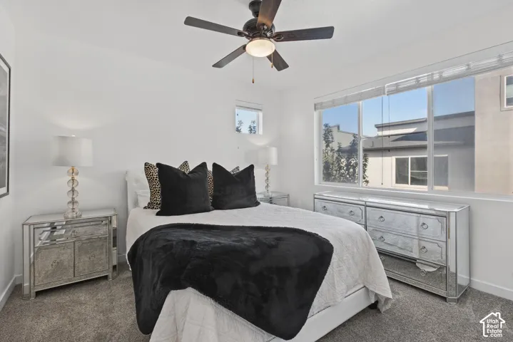 Bedroom featuring wall-to-wall carpeting, a multi-pane window with integrated blinds, a central ceiling fan with an integrated light fixture, and an additional small transom window