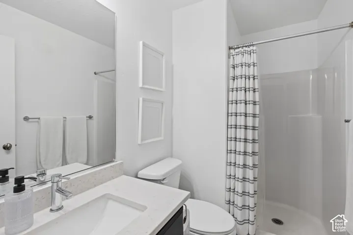 Bathroom featuring a vanity with a light-toned countertop, integrated rectangular sink, chrome single-handle faucet, large frameless wall-mounted mirror, and a curved shower enclosure