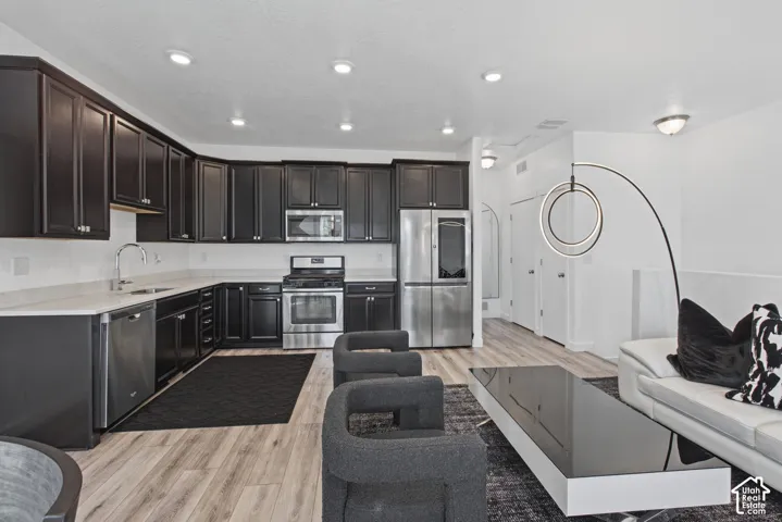 Kitchen featuring dark cabinetry, solid-surface countertops, wood-finish flooring, stainless steel appliances, and recessed ceiling lighting