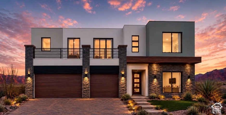 Modern exterior featuring multi-tonal stucco siding, stone veneer accents, wood-finish garage doors, a second-story balcony with horizontal metal railings, and integrated wall-mounted lighting