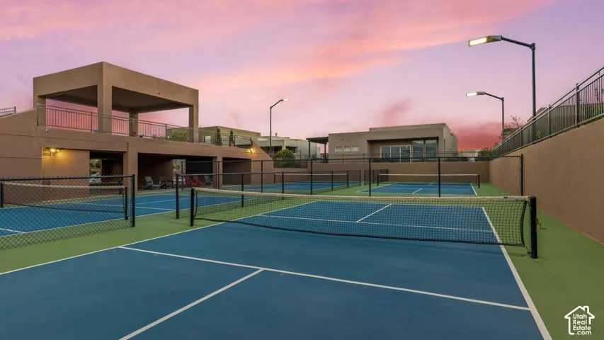 Multi-court athletic facility featuring hard-surface tennis and pickleball courts, perimeter chain-link fencing, stadium-style lighting, and a tiered concrete viewing deck