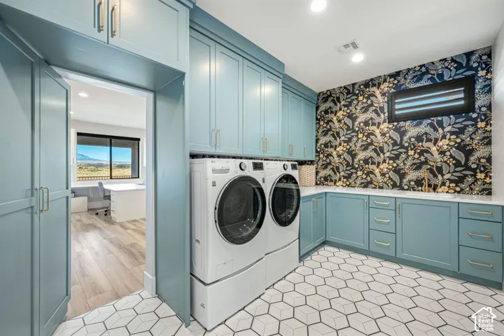 Custom blue cabinetry with gold-tone hardware, white countertops, geometric tile flooring, patterned wallpaper accent wall, and a drop-in sink