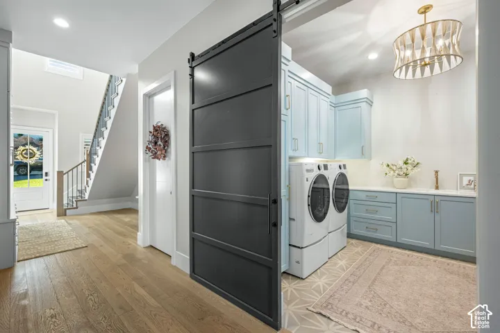 Laundry room featuring a sliding matte black barn door, custom cabinetry in a soft blue finish, patterned tile flooring, and a decorative pendant light fixture