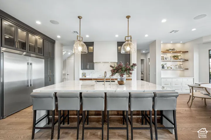 Kitchen featuring a central island with a stone countertop, full-height dark-toned cabinetry, dual glass pendant lights, recessed ceiling lighting, and wood-finish flooring