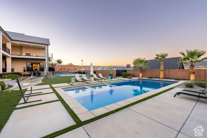 Backyard featuring an in-ground swimming pool with integrated spa, large-format concrete pavers, artificial turf, and a masonry perimeter wall