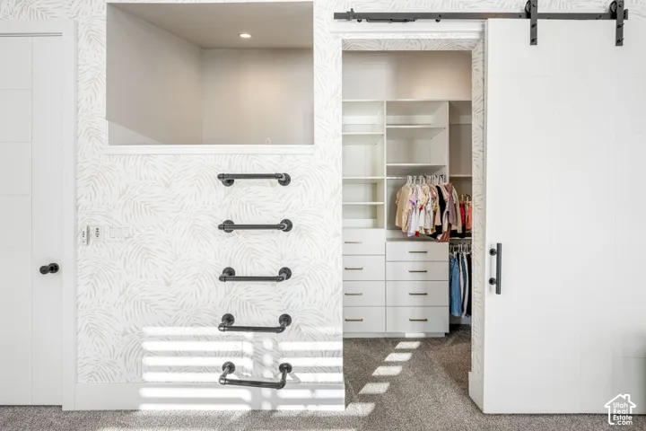 Custom walk-in closet featuring white built-in shelving and drawers, a sliding barn door with matte black hardware, patterned wallpaper, and a built-in climbing ladder