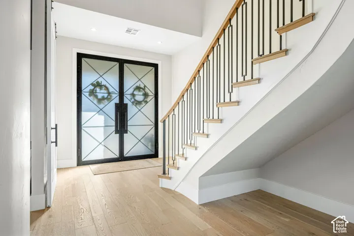 Foyer entry featuring a double glass door with geometric metal framing, wood-finish flooring, and a curved staircase with a custom metal railing and wood-capped steps