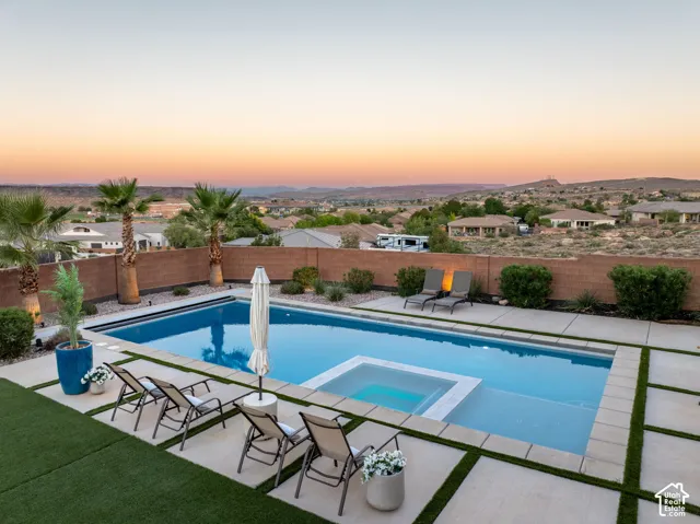In-ground swimming pool with an integrated spa, surrounded by a concrete paver patio and artificial turf lawn, enclosed by a masonry perimeter wall, accented by mature palm trees