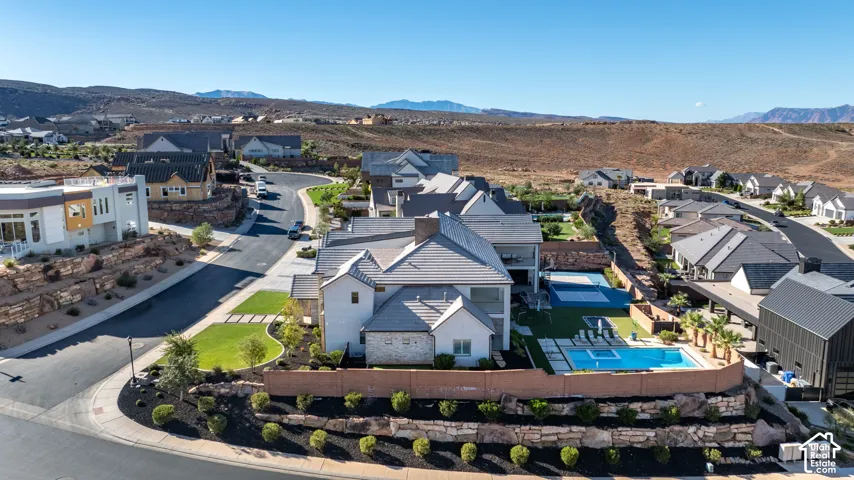 Aerial perspective featuring a multi-story residence with a tile roof, an in-ground swimming pool, a dedicated sport court, and tiered stone retaining walls