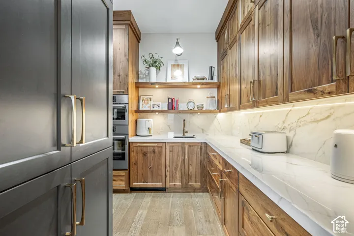 Kitchen featuring custom walnut cabinetry, stone slab backsplash, quartz countertops, built-in double ovens, and wood-finish flooring