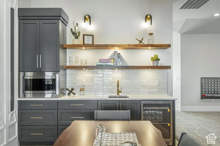 Charcoal cabinetry with brushed metallic hardware, integrated stainless steel microwave, stone-finish countertops, subway tile backsplash, and tiered natural wood shelving with recessed under-cabinet lighting