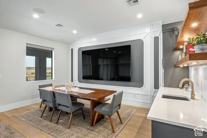 Custom millwork media wall with integrated paneling, wood-finish flooring, floating wood shelving with under-cabinet lighting, quartz countertop, and undermount bar sink