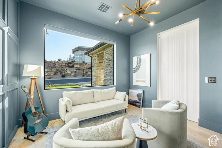 Room featuring floor-to-ceiling wall paneling, expansive picture window, modern sputnik chandelier, and light wood-finish flooring
