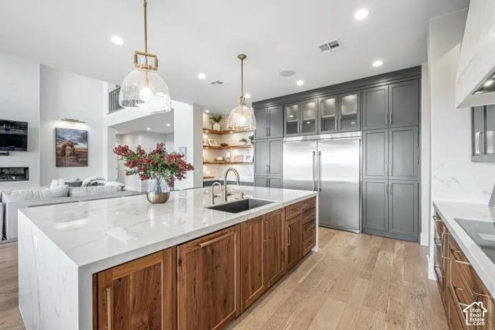 Kitchen featuring a stone-surface waterfall island with a stainless steel undermount sink, custom wood-finish cabinetry, floor-to-ceiling charcoal cabinetry, stainless steel refrigerator, and recessed lighting
