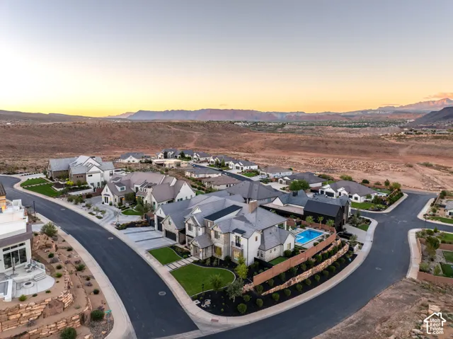 Aerial view of the residential property featuring stone and stucco exterior construction, a private swimming pool, concrete hardscaping, manicured lawn areas, and mountain scenery