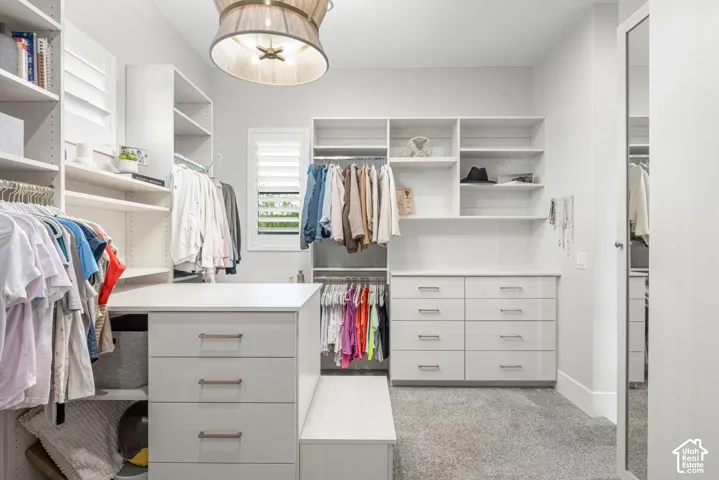 Walk-in closet featuring custom white built-in cabinetry, integrated drawer banks, adjustable open shelving, and a decorative drum pendant light fixture