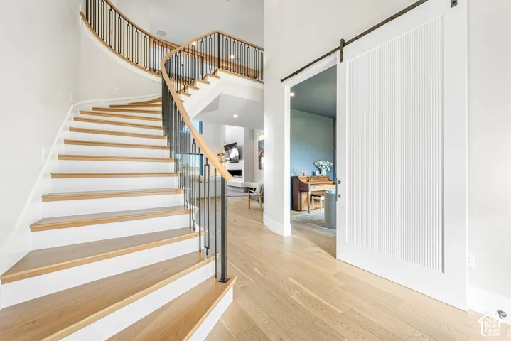 Curved staircase featuring wood-finish treads and a metal spindle railing, complemented by wide-plank wood-finish flooring and a white vertical-paneled sliding barn door