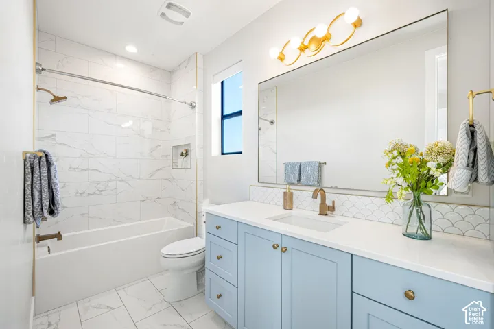 Bathroom featuring light blue cabinetry, white quartz vanity countertop with an undermount sink, scallop-patterned tile backsplash, large rectangular wall mirror, and shower-tub combination with stone-patterned tile surround