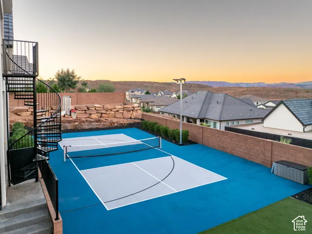 Multi-sport court with a paved surface, black metal spiral staircase, natural stone retaining wall, and mountain backdrop