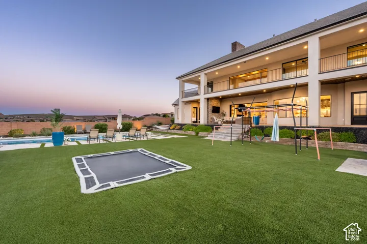Multi-level exterior featuring stucco siding, double-tiered covered balconies with metal railings, a paved pool deck, and a synthetic turf lawn